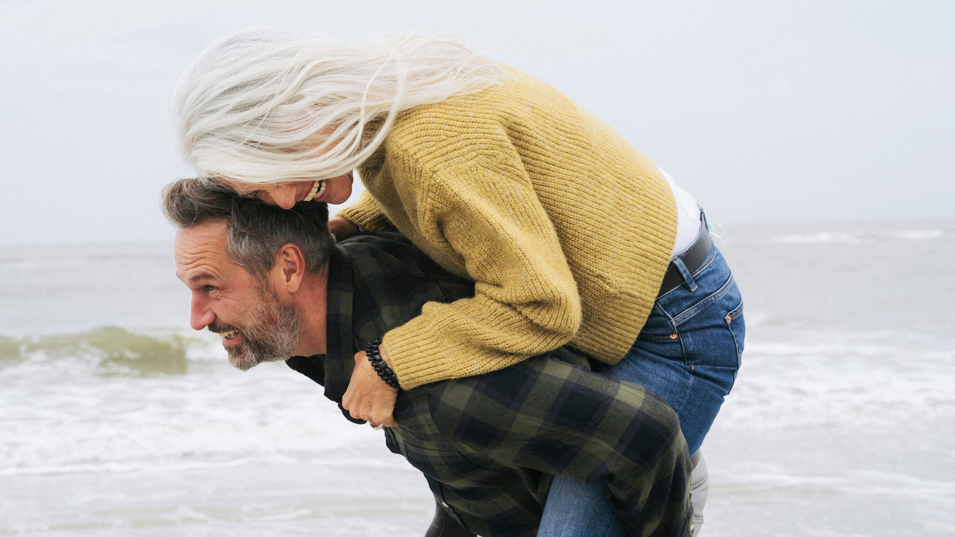 Mann i 50 årene bærer en kvinne på ruggen på samme alder på stranden