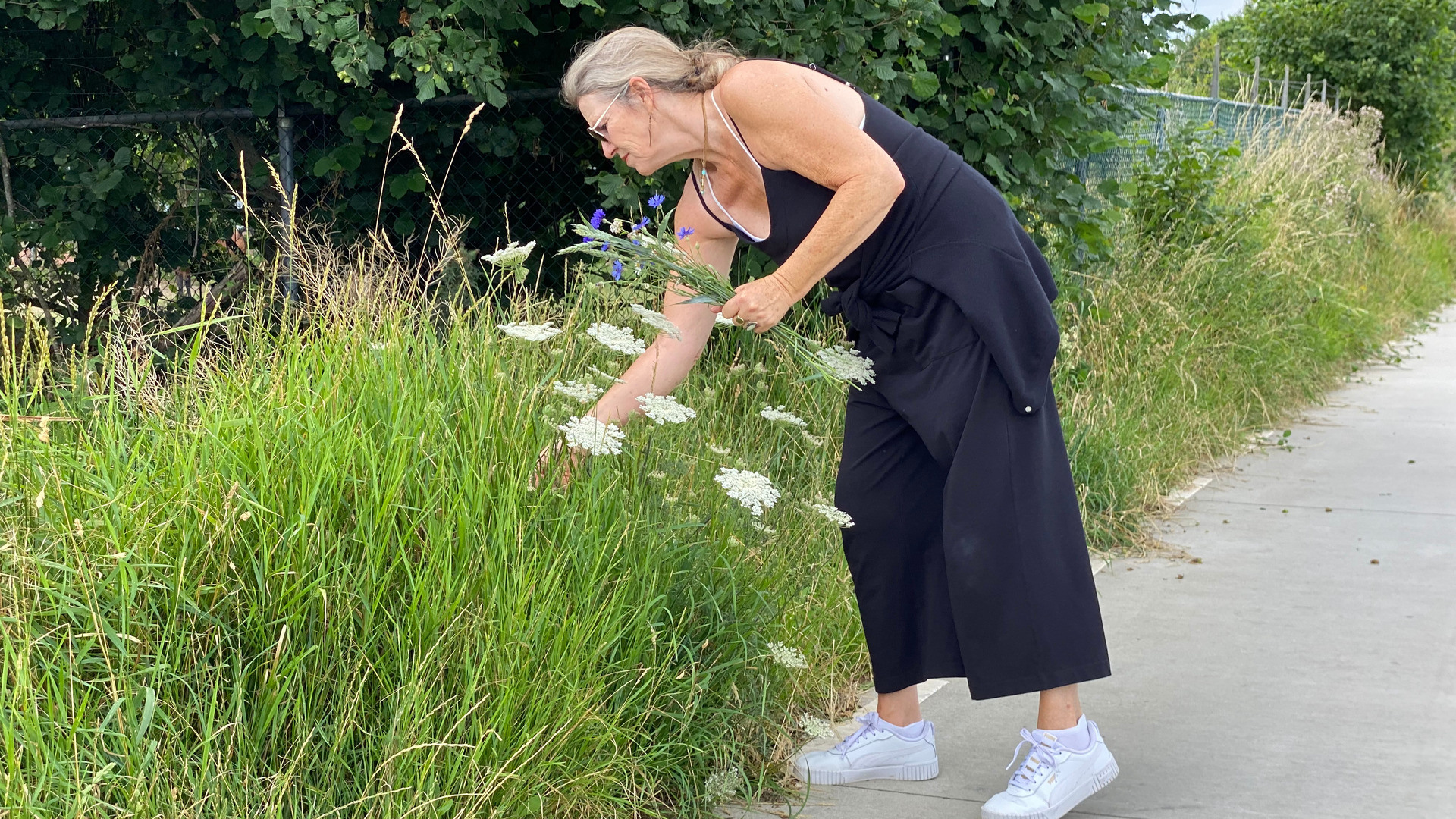 Kvinne i sommerkjole plukker blomster langs veikanten