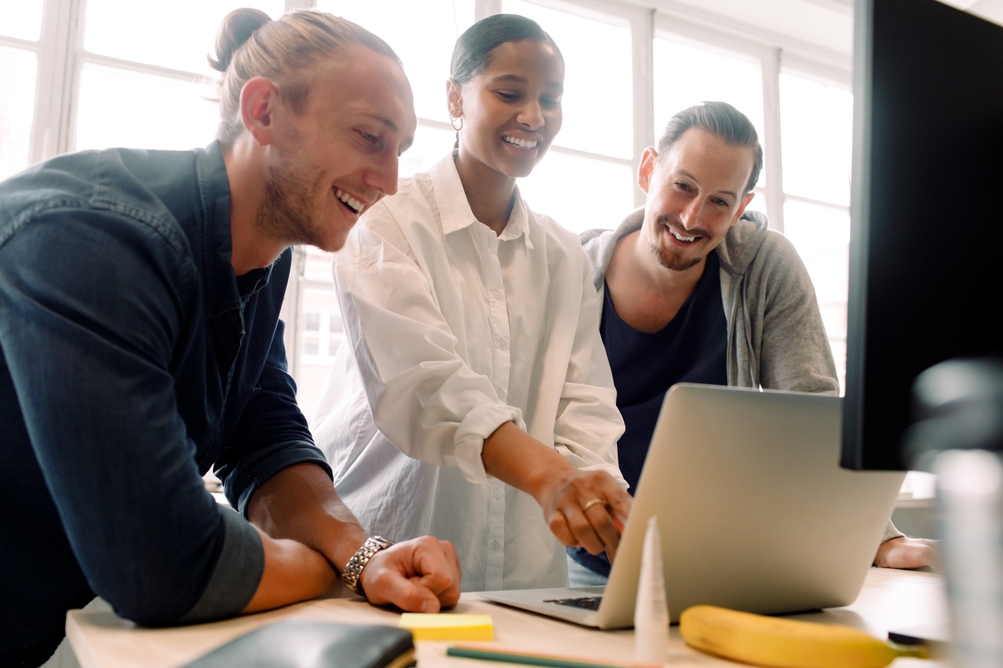 Tre unge kolleger står rundt en PC og ser på skjermen og smiler